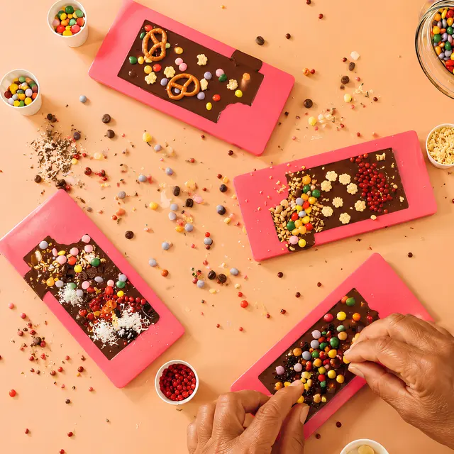 Mehrere Schokoladentafeln werden mit bunten Süßigkeiten, Nüssen und Dekorationen verziert.