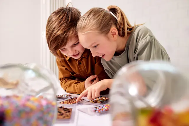 Zwei Kinder betrachten und verzieren Schokoladentafeln mit bunten Süßigkeiten und Streuseln. Das Foto basiert auf einer realen Aufnahme und wurde mit Unterstützung künstlicher Intelligenz hinsichtlich Farben, Lichtstimmung und Bildqualität optimiert.